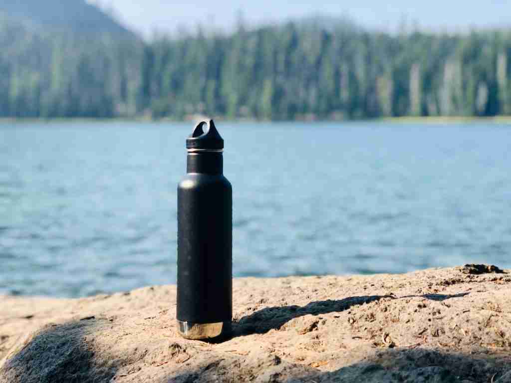 black and gray sports bottle on brown sand near body of water during daytime