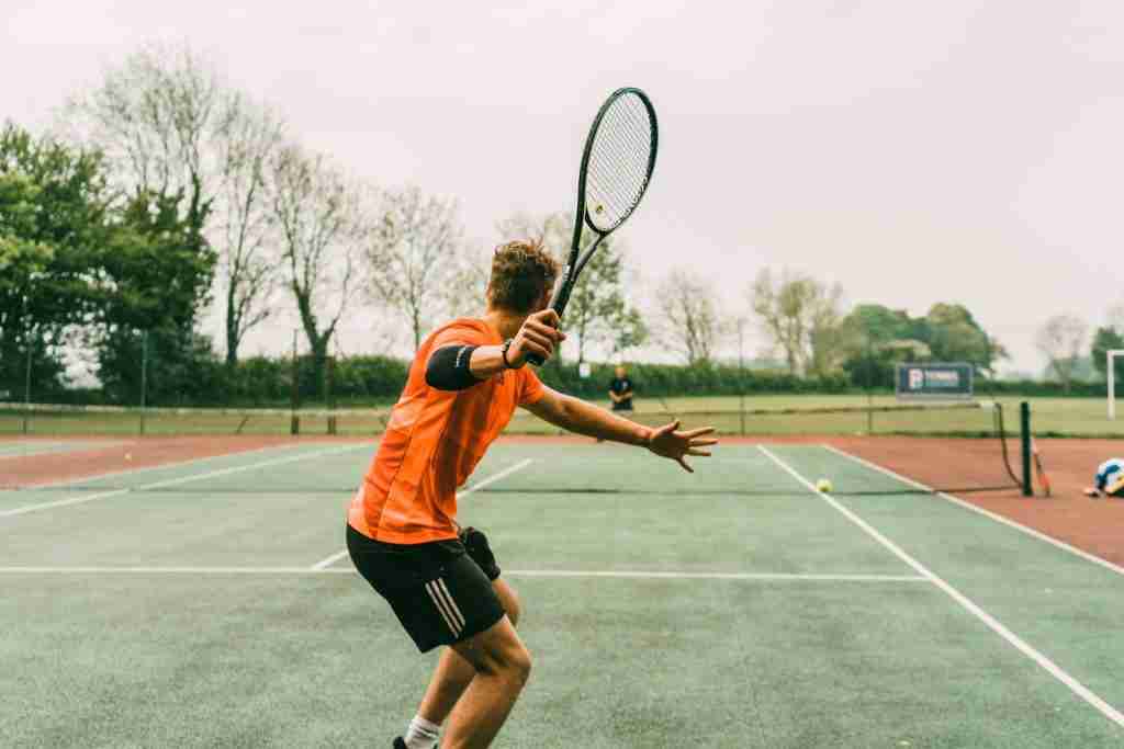 man in orange shirt and black shorts holding black and white tennis racket