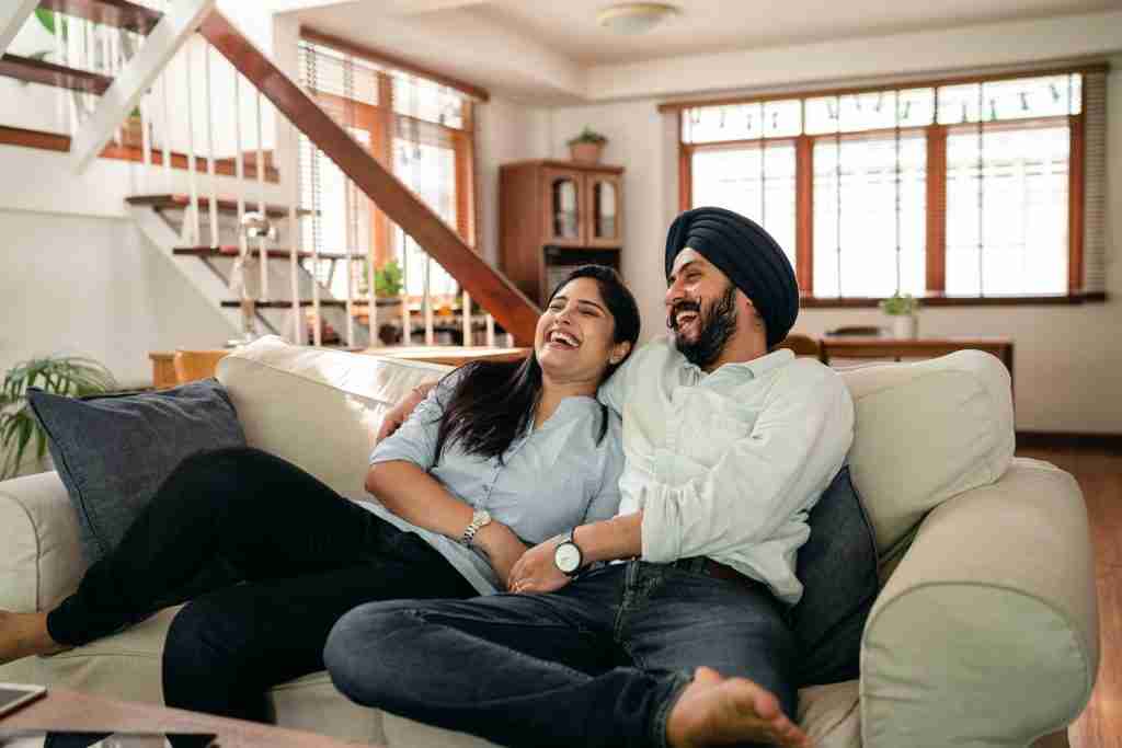 Laughing young Indian couple exploring fun facts about Gemini while watching a comedy at home.