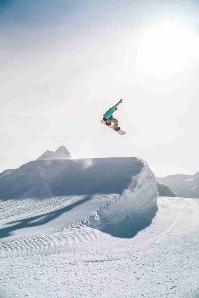 man in black jacket and blue denim jeans jumping on snow covered mountain during daytime