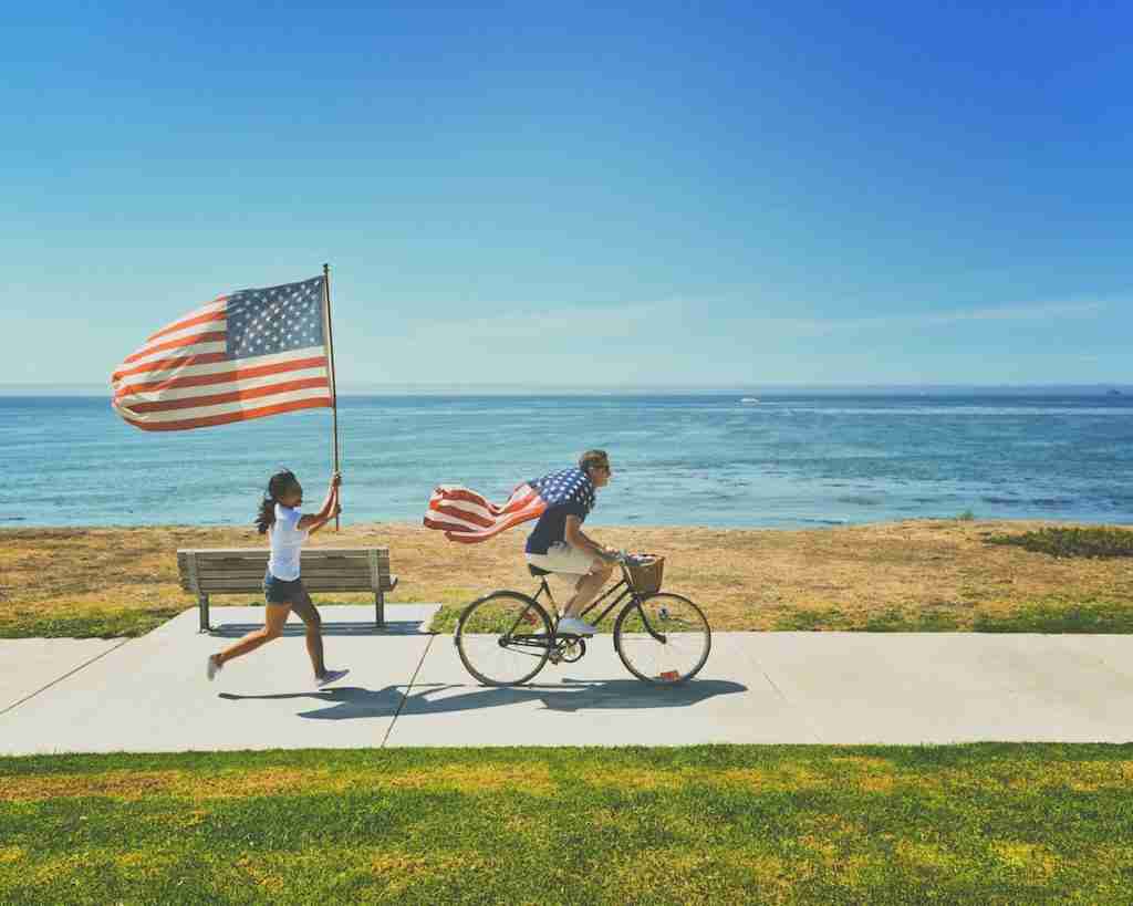 A man riding a bike and a woman running while holding the USA flag, embodying the spirit of fun facts about the USA.