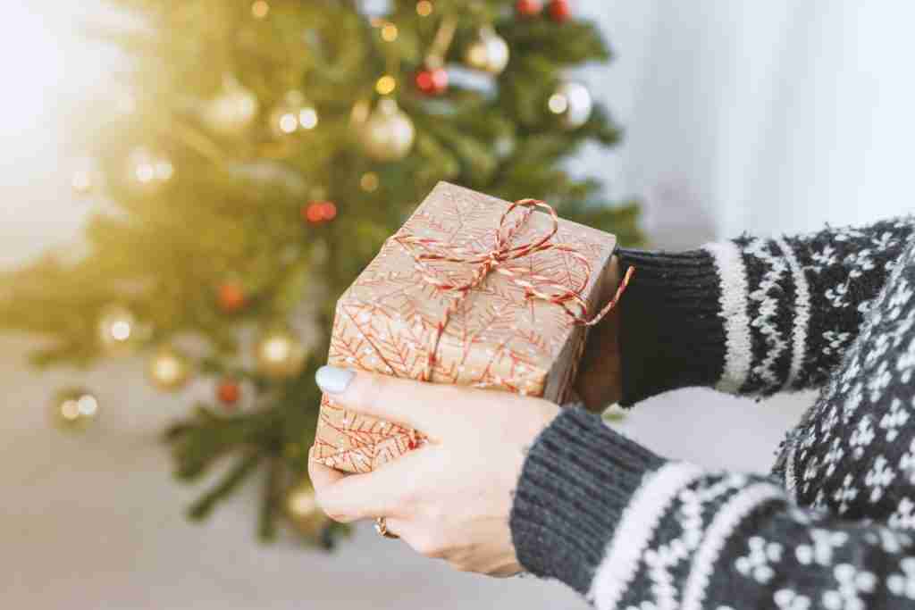 A person holding a gift box in front of a Christmas tree, showcasing interesting facts about Christmas.