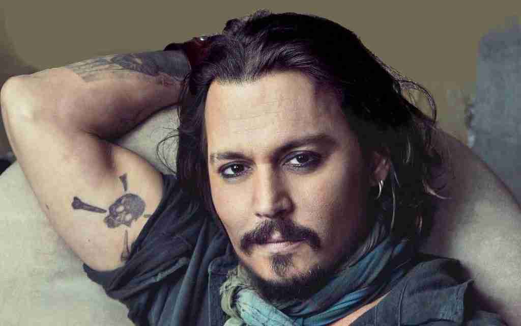 Johnny Depp posing for  a photo with long hair and a tattoo on arm showcasing fun facts about Johnny Depp