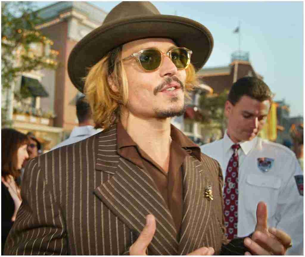 Johnny Depp posing for a photo in brown suit with matching glasses and a hat.